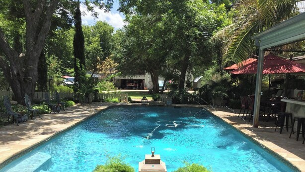 A rectangular swimming pool with a stone deck, surrounded by trees and outdoor furniture.