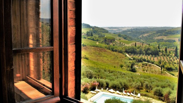 A view from a window overlooking a pool area with a vineyard landscape.