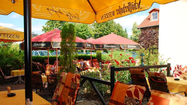 An outdoor seating area with tables and chairs under yellow umbrellas, some with 'Köstritzer' branding. - Aragon am Lennepark (Ahrensfelde)