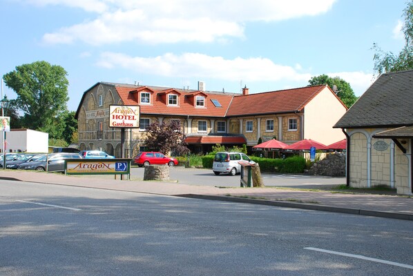 A hotel with a red-tiled roof, a signboard, and a parking area.