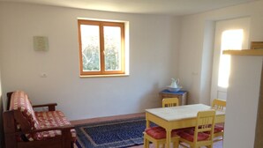 Ein Zimmer mit Esstisch, Stühlen, einer Couch, einem Teppich und einem Fenster.