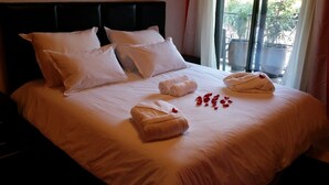 A neatly made bed with white linens and towels, a black headboard, and a view of potted plants through a window. - Elegant Gueliz Retreat near Majorelle (Marrakech)