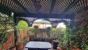 An outdoor patio with a table and chairs, surrounded by potted plants and a lattice structure overhead. - Elegant Gueliz Retreat near Majorelle (Marrakech)