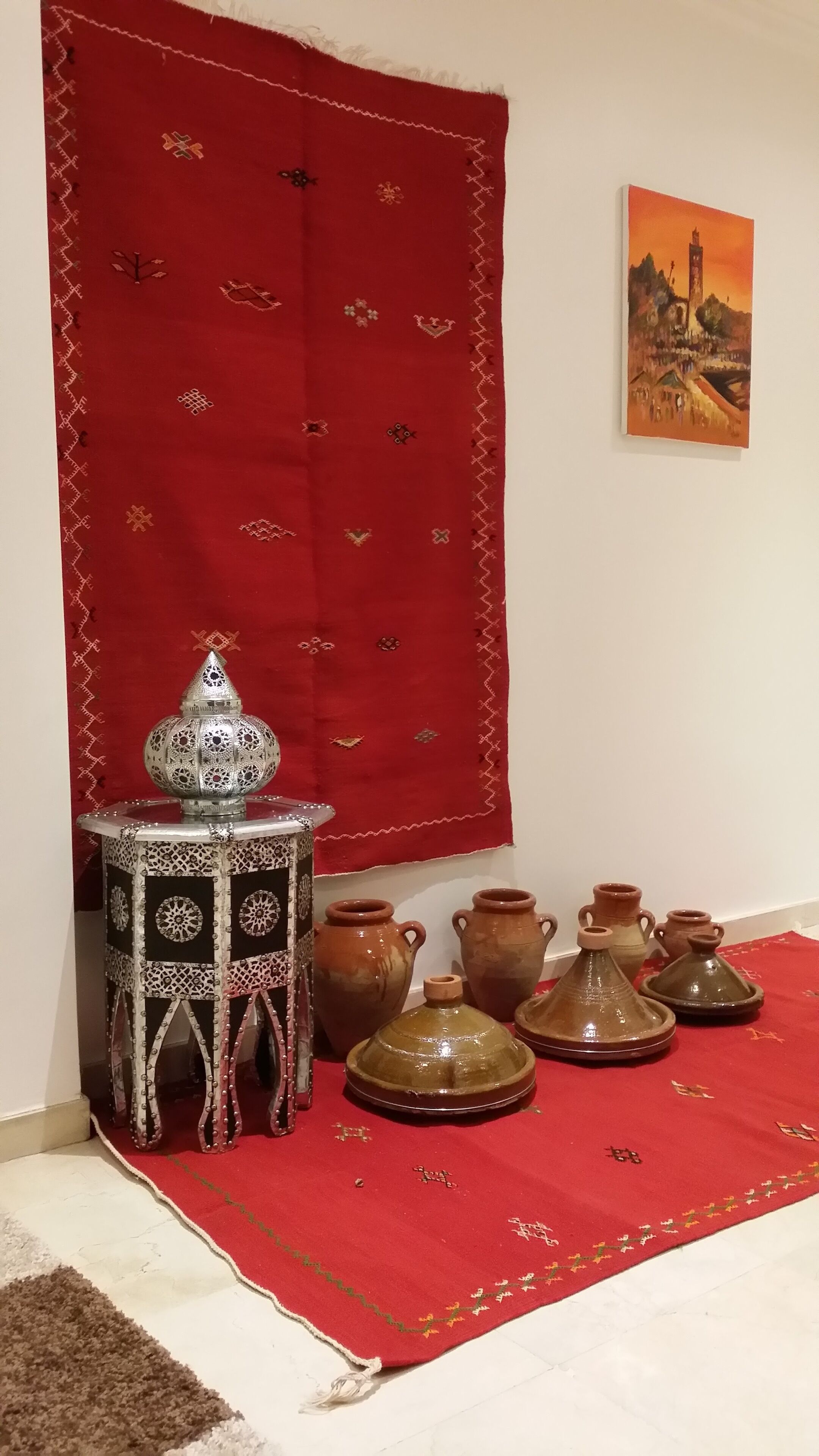 A room with a red carpet, a patterned rug, a decorative metal stand, and several clay pots.