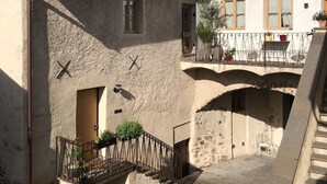 Ein Innenhof mit Kopfsteinpflasterweg, einer kleinen Brücke und Gebäuden mit Balkonen und Blumentöpfen.