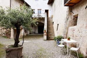 A courtyard with a cobblestone floor, a potted tree, a white table with chairs, and a staircase leading to an upper level. - Casa Jenner - historic house next to the center (Appiano S.S.D.V.)