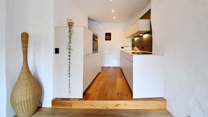 Eine schmale, moderne Küche mit weißen Schränken, Holzboden und einer großen Vase auf der linken Seite.