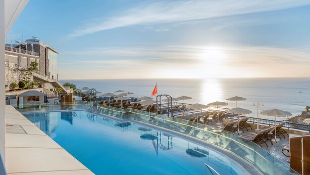 Zona junto a la piscina con sillas de descanso y sombrillas, con vista al mar.