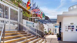 Entrada de hotel con escaleras, varias banderas y un letrero de 'Bienvenido'.