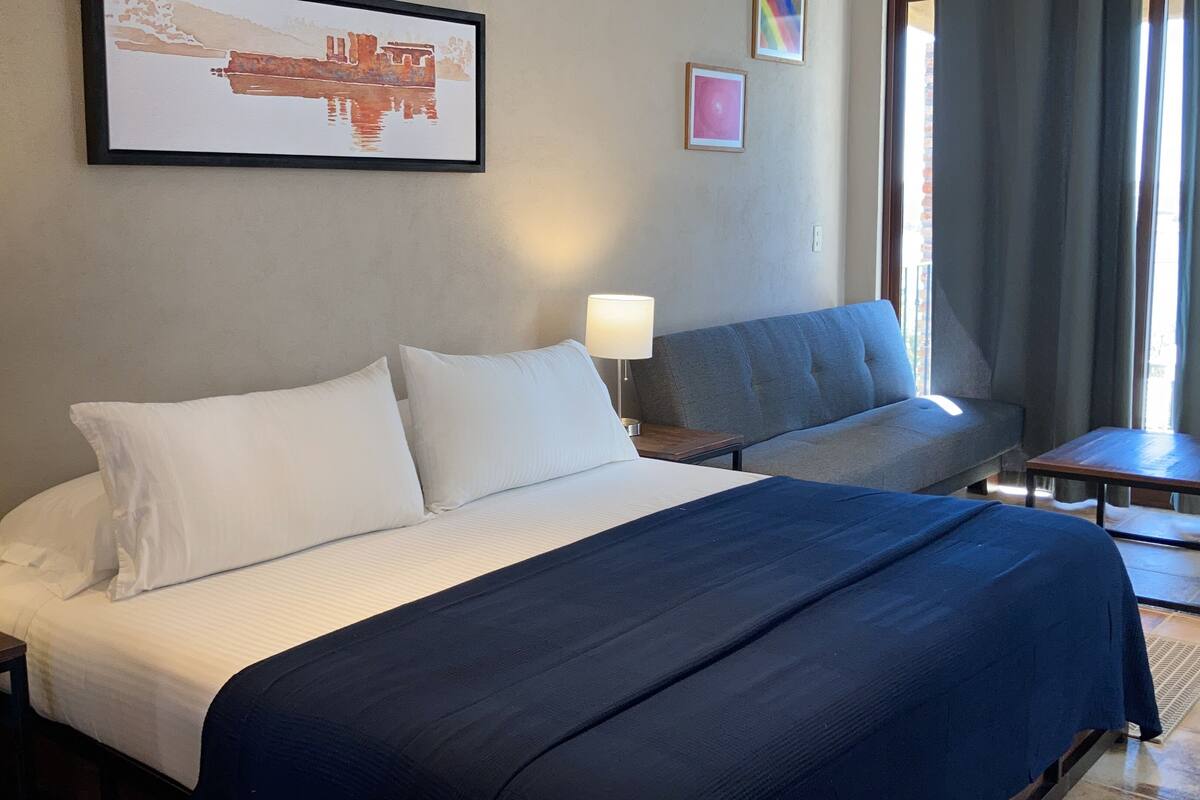 Una habitación de hotel con una cama grande, dos mesitas de noche, un sofá y un cuadro en la pared.