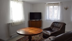 Een woonkamer met een bruine leren bank, een houten salontafel, een flatscreen televisie op een houten kast en een kamerbreed tapijt met een patroon.