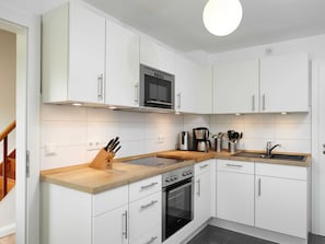 Una cocina moderna con armarios blancos, encimera de madera, horno empotrado, microondas y pileta.