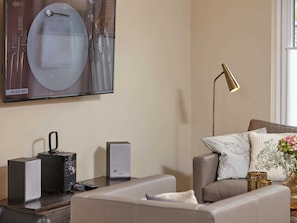 Una sala de estar moderna con un sofá, una mesa de centro, un televisor de pantalla plana montado en la pared, una lámpara de pie y un jarrón decorativo con flores.
