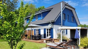 A two-story house with a blue exterior, a deck, outdoor seating, and a barbecue area.