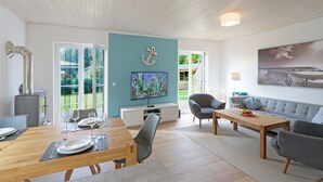 A spacious living area with a dining table set for four, a comfortable sofa, and a flat-screen TV mounted on a teal wall.
