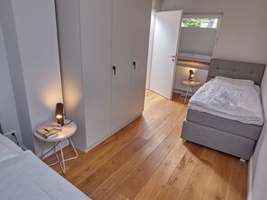 A bedroom with a bed, a bedside table with a lamp, a wardrobe, and a window with blinds. - 5 * Holiday home Düneneck 10 - Holiday home Düneneck 10 (Sankt Peter-Ording)
