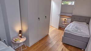 A bedroom with a bed, a bedside table with a lamp, a wardrobe, and a window with blinds. - 5 * Holiday home Düneneck 10 - Holiday home Düneneck 10 (Sankt Peter-Ording)