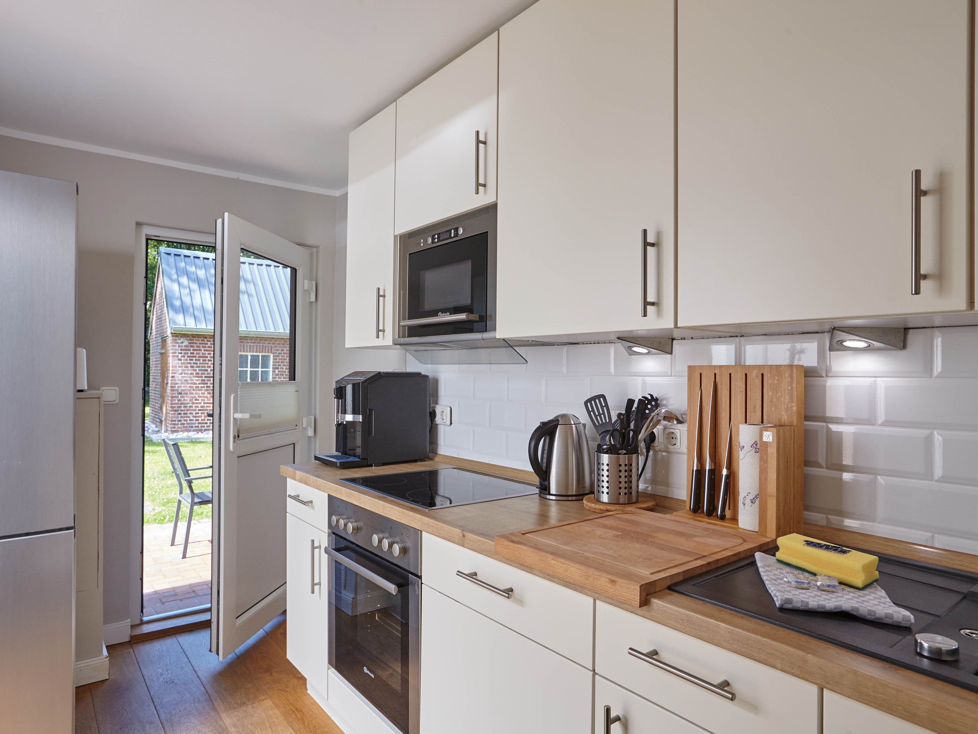A modern kitchen with white cabinets, a built-in microwave, a coffee machine, and a wooden countertop.