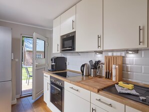 Una cocina moderna con armarios blancos, microondas integrado, cafetera y encimera de madera.