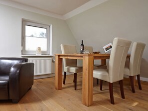 Un comedor con una mesa de madera, cuatro sillas, un sillón de cuero negro, un radiador y una ventana con persianas.