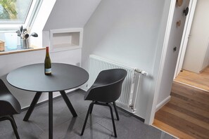 Una habitación moderna con una mesa redonda, dos sillas negras, una botella de vino, una ventana con vistas y un radiador blanco.