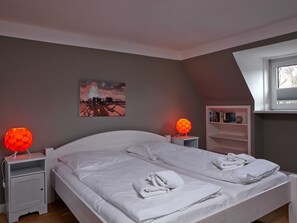 Un dormitorio con una cama, dos mesitas de noche, una estantería con libros y un cuadro en la pared.