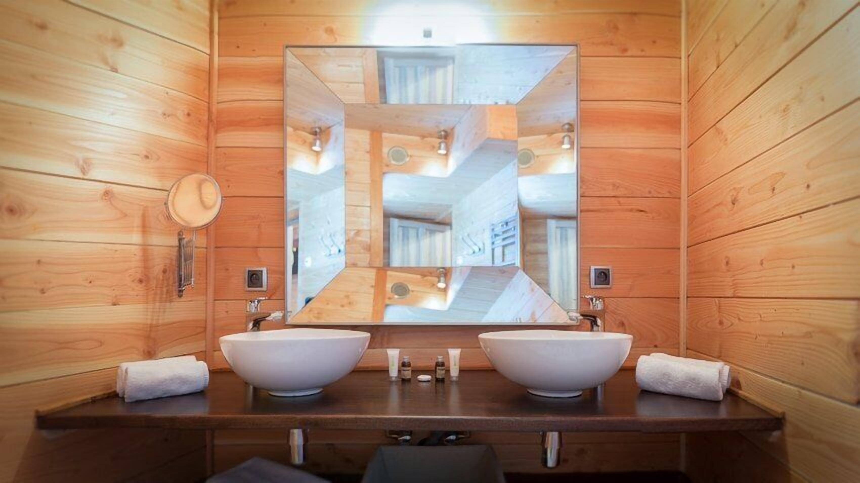 Un baño de cabaña de madera con dos lavamanos grandes, un espejo y un perchero para toallas.