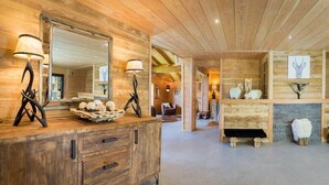 L’intérieur d’un chalet en bois, avec un grand miroir, deux lampes, une commode en bois et une cheminée en pierre.