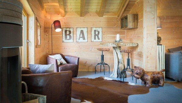 Un intérieur rustique en bois, avec une cheminée, des meubles en cuir, un tapis en peau de vache et une enseigne sur laquelle on peut lire « BAR ».