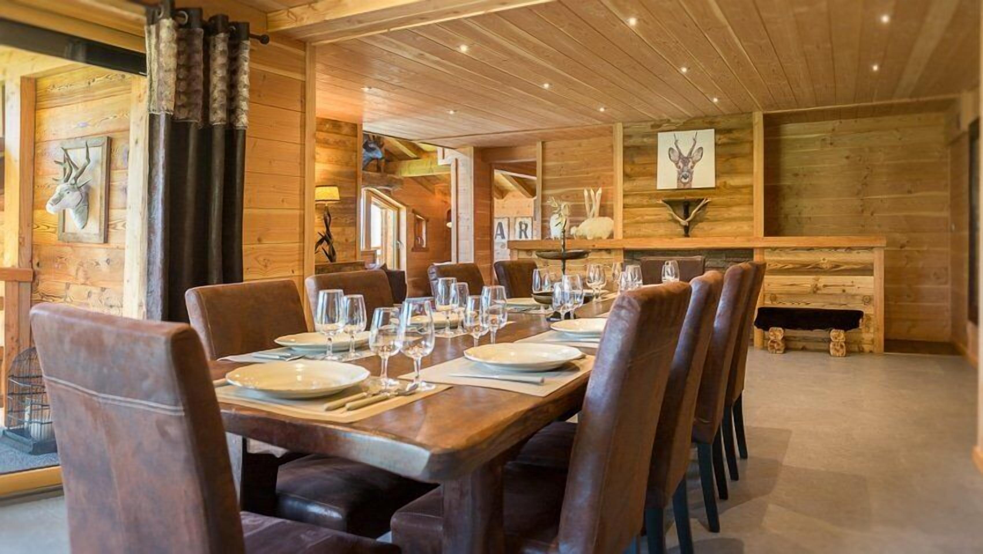 A dining area with a long wooden table set for a meal, surrounded by leather chairs.