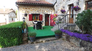 A stone house with a green lawn, a dining table, and red shutters.
