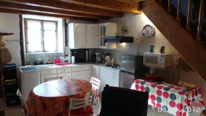 A kitchen with wooden beams, white cabinets, a microwave, and a dining table with a polka dot tablecloth.