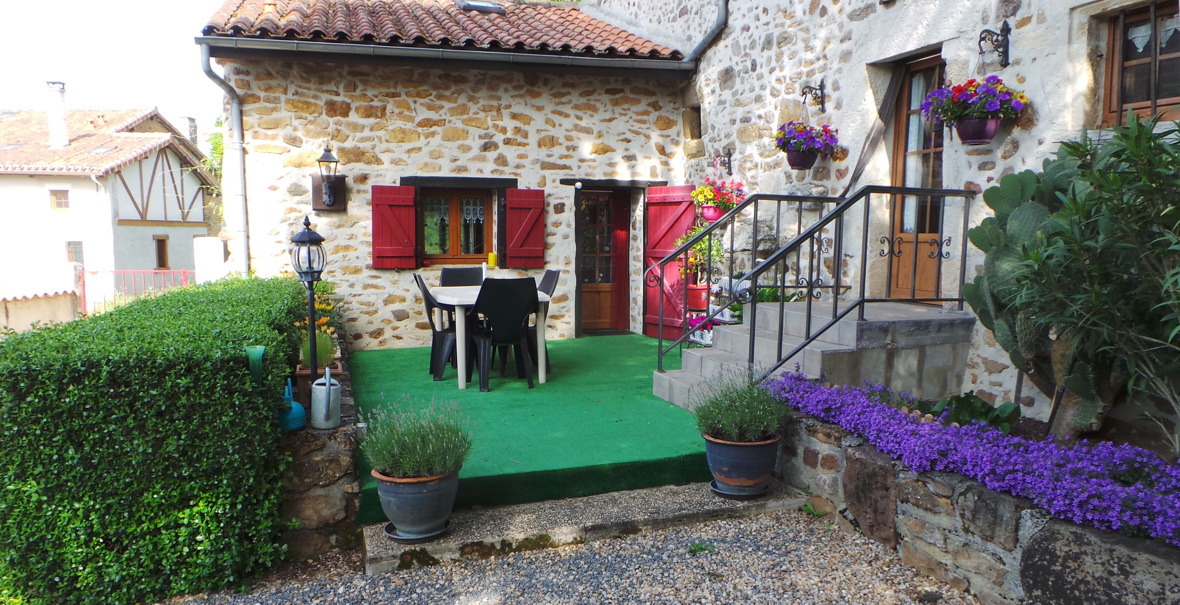 Una casa de piedra con un césped verde, una mesa de comedor y contraventanas rojas.