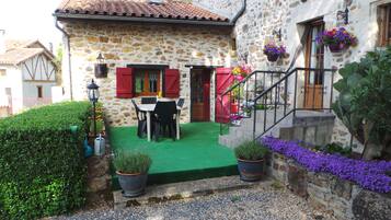 Una casa de piedra con un césped verde, una mesa de comedor y contraventanas rojas.
