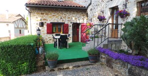 A stone house with a green lawn, a dining table, and red shutters.