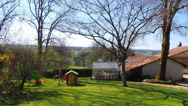 A rural setting with a green lawn, a small wooden structure, and a building with a tiled roof.