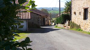 A narrow rural road flanked by stone buildings with tiled roofs.