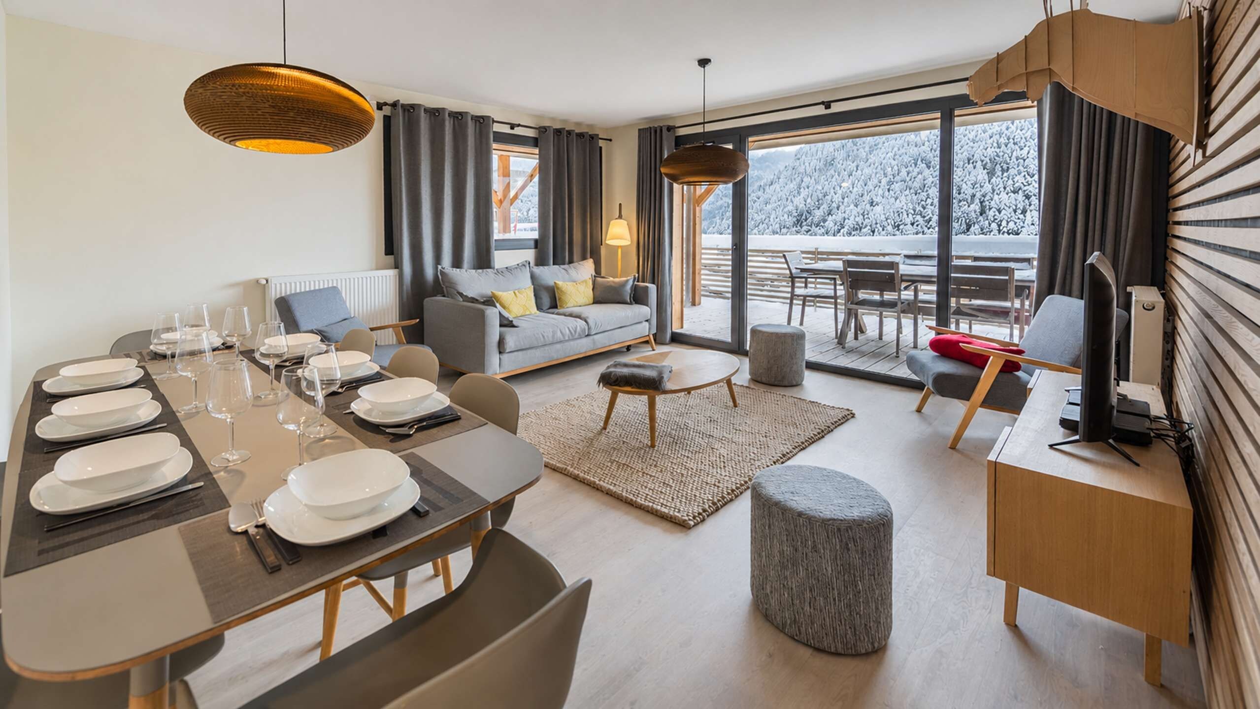 A modern dining area with a table set for four, a sofa, and a view of a snowy landscape through large windows.