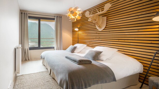 Una camera da letto moderna con un ampio letto, testiera in listelli di legno e vista sulle montagne.