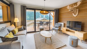 A modern living room with a sofa, coffee table, TV, and a view of an outdoor deck. - 6-person flat - modern, central, ski in, ski out (Châtel)
