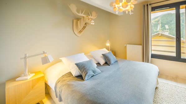 A bedroom with a bed, bedside tables, a mounted deer head, a window with a view of a building, and a chandelier. - 6-person flat - modern, central, ski in, ski out (Châtel)