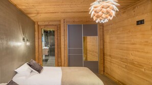 A wooden-paneled room with a bed, a bathroom visible through a glass door, and a unique ceiling light fixture. - Luxurious chalet - close to the centre, private sauna and spa, large open spaces (Châtel)