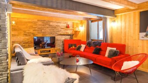 A cozy living room with a stone wall, a red sofa, a TV, and a fireplace. - Luxurious chalet - close to the centre, private sauna and spa, large open spaces (Châtel)