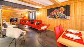 Ein modernes Wohnzimmer mit einem roten Sofa, einem Esstisch für zwei Personen und einem farbenfrohen Bärenbild an der Wand.