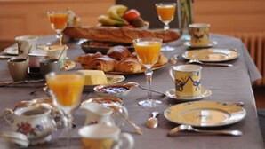 Une table de petit-déjeuner dressée avec des croissants, des fruits, du jus d’orange et du café.