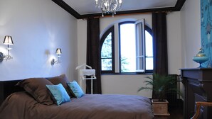 Une chambre à coucher avec un grand lit, une table de chevet, une commode, une fenêtre avec des rideaux et un lustre.