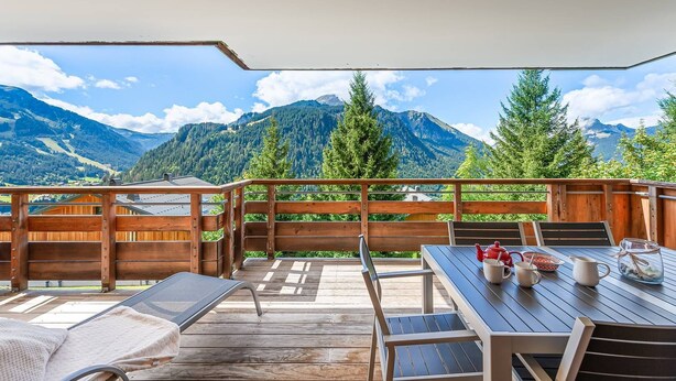 An outdoor deck with wooden furniture, a table with cups and a teapot, and a view of mountains. - Luxury flat 6 pers. - fireplace, close to the centre and slopes (CHATEL)