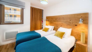 A hotel room with two beds, wooden headboards, a window with a view of a building, and a radiator. - Luxury flat for 8 people - modern, close to the centre and slopes (CHATEL)