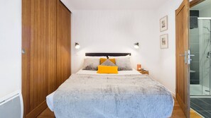 A bedroom with a bed, wooden wardrobe, bedside table, and a glass shower enclosure.