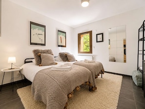 A bedroom with two beds, a round side table, a lamp, and a large mirror.